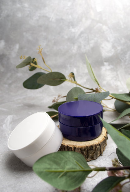 两罐面霜放在一个木架上，围绕着桉树的树叶和树枝。图片下载