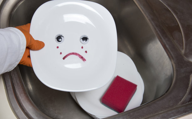 厨房水槽里洗得不干净的盘子。女人手捧着白色的盘子，眼睛里流露着悲伤的情绪。图片下载