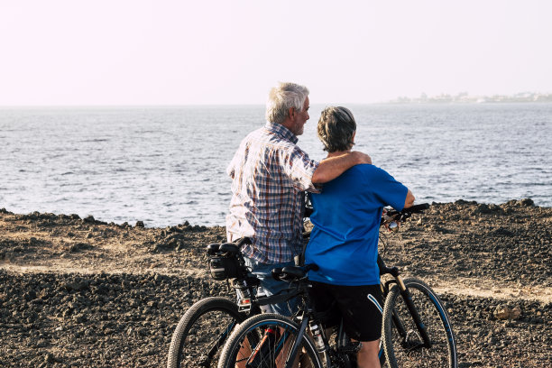 一对漂亮的老夫妇在海滩或公园里骑着他们的自行车拥抱在一起——成熟和活跃的人们正在努力锻炼身体图片下载