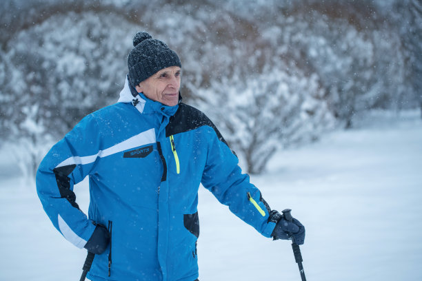 在冬天的森林里，穿着暖和衣服的老人拿着北欧棍棒站在那里图片下载