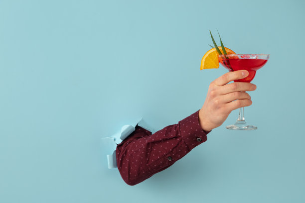 男手与鸡尾酒杯打破蓝色纸背景。图片下载