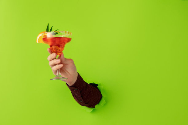 男手拿着鸡尾酒杯打破绿纸背景。图片下载