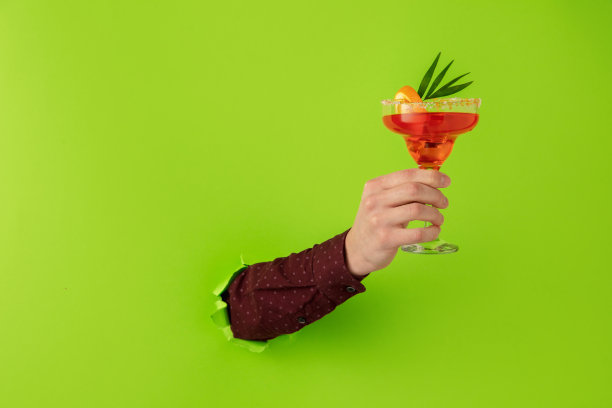 男手拿着鸡尾酒杯打破绿纸背景。图片下载