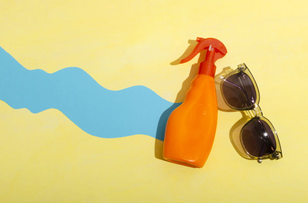 俯视图装饰蓝色波浪纸，玻璃和橙色瓶子的太阳霜在黄色的背景图片下载