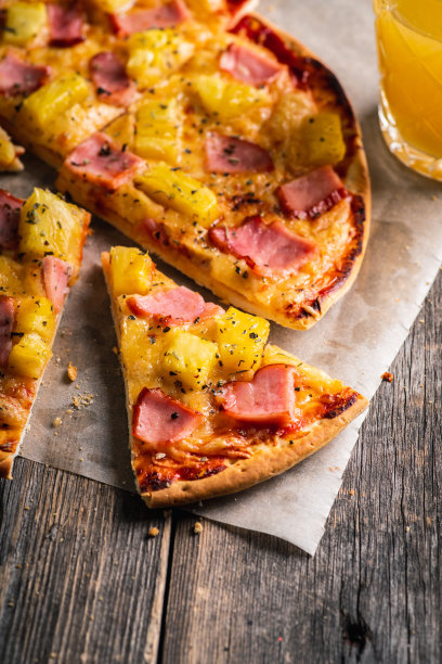 刚烤过的夏威夷披萨配上新鲜切好的菠萝和火腿，点缀在质朴的木质背景上。有选择性的重点。图片下载