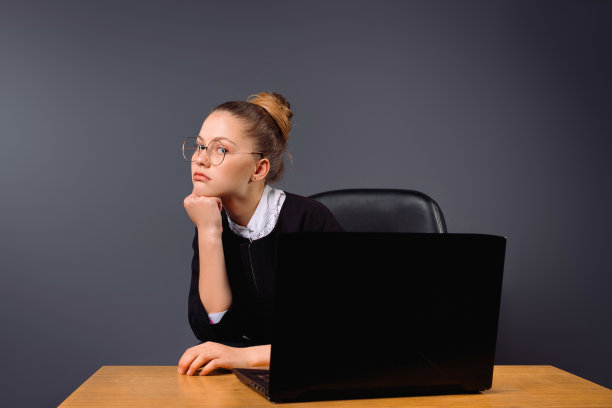 在灰色的雾霾中，一位沉思的女商人坐在电脑前的皮质扶手椅上。图片下载