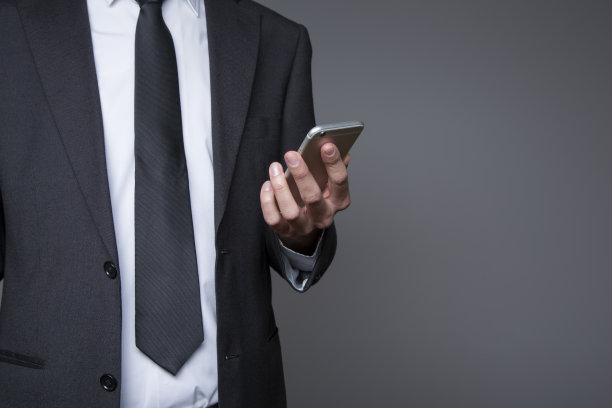 灰色背景下穿着灰色西装的商人手里拿着手机图片下载