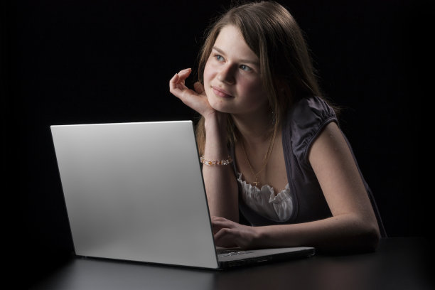 一头棕色长发的年轻女孩向手提电脑走来图片下载