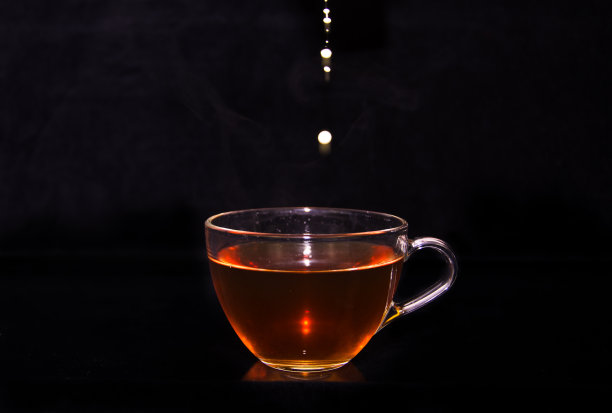 白色的牛奶奶油倒进一杯茶中，在黑色的背景前形成一些水滴、气泡和云彩图片下载