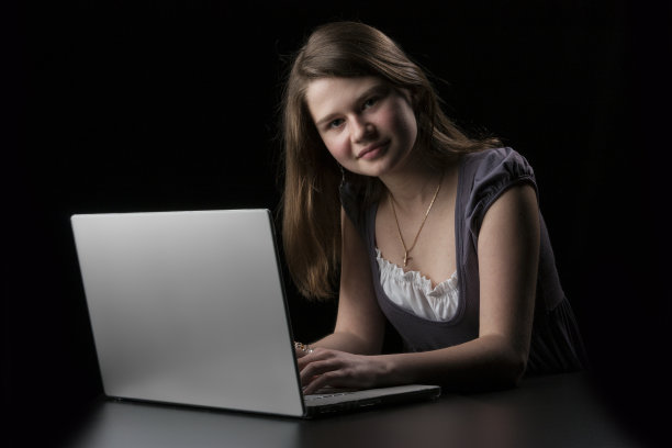 一头棕色长发的年轻女孩向手提电脑走来图片下载