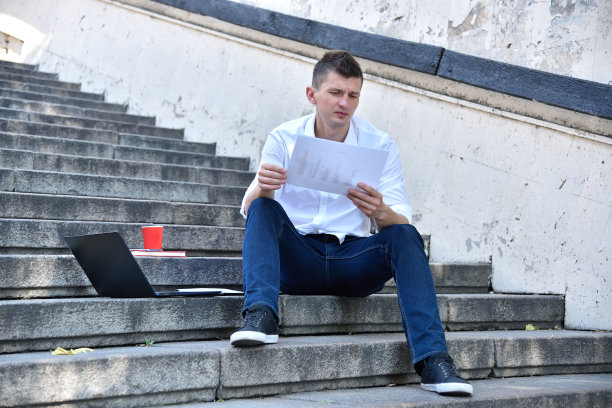 年轻商人拿着财务文件坐在楼梯上。图片下载