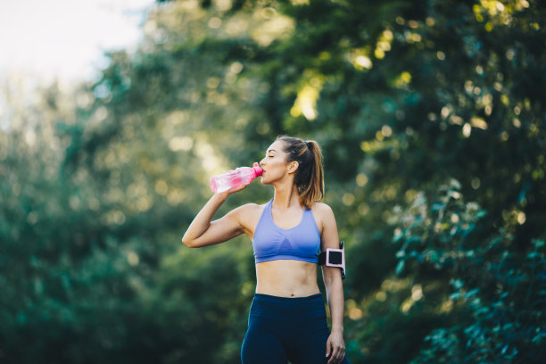 年轻女子正在喝瓶子里的水，正在慢跑休息。图片下载