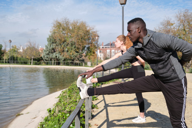 非洲黑人男人和红发白人女人在公园里伸展他们的腿。户外健身和运动。图片下载