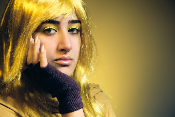一个戴着金色假发的年轻女孩看着镜头，她的脸搁在戴着手套的手上图片下载