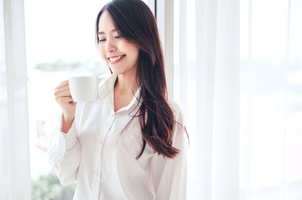 快乐的亚洲妇女在白色卧室里手捧咖啡杯图片下载