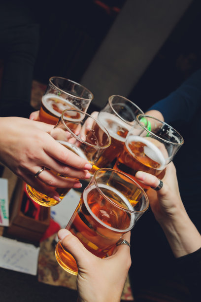 朋友们拿着啤酒杯围坐在咖啡吧的桌子旁欢呼——一群不同种族的人在酒吧里互相敬酒碰杯。图片下载