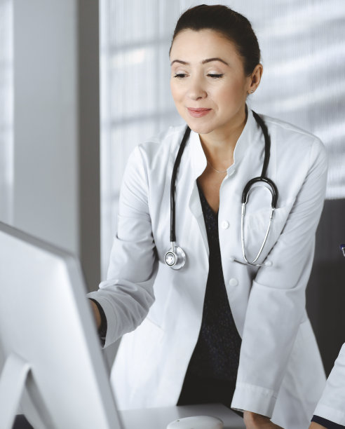 两个女医生正在讨论药物治疗，而站在桌子上在一个诊所的办公室。医生在工作中使用电脑。团队合作在医学图片下载