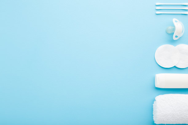 在蓝色的桌子背景上放一排白色的清洁棉垫、清洁棒、毛巾、乳膏管和奶嘴。柔和的颜色。特写镜头。婴儿日常卫生用品。文本的空位置。自顶向下的观点。图片下载