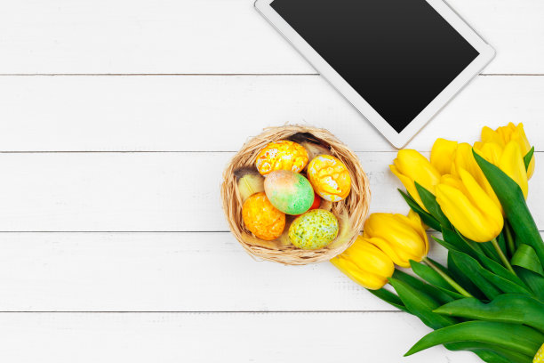 平板电脑屏幕上的信息和彩色郁金香和复活节彩蛋的木制背景图片下载