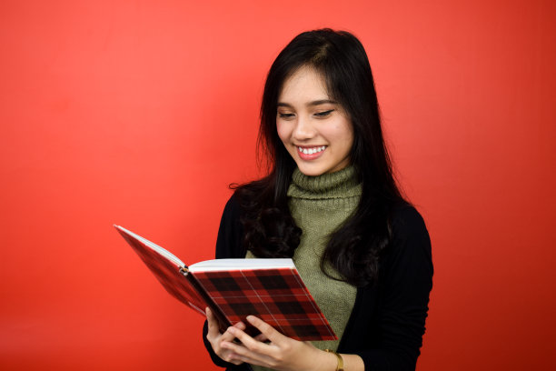 拿着书读年轻美丽的亚洲妇女用黑色毛衣与红色孤立的背景图片下载