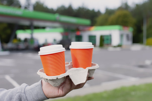 一个男人在加油站手里拿着两杯咖啡。图片下载