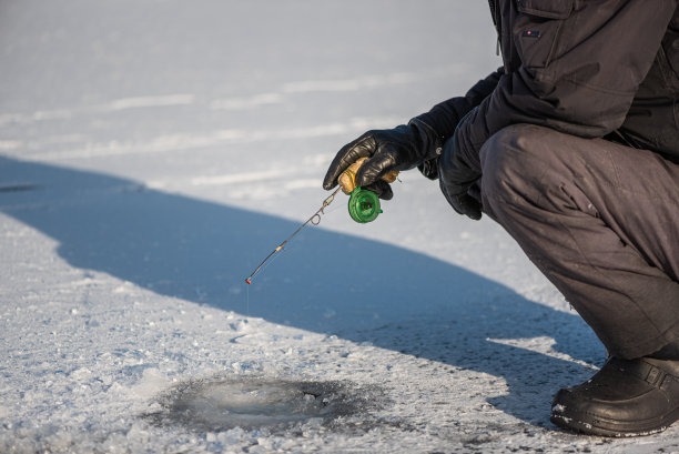 在阳光明媚的霜天，冰上钓鱼。坐在冰洞附近捕鱼的人。冬季活动。图片下载
