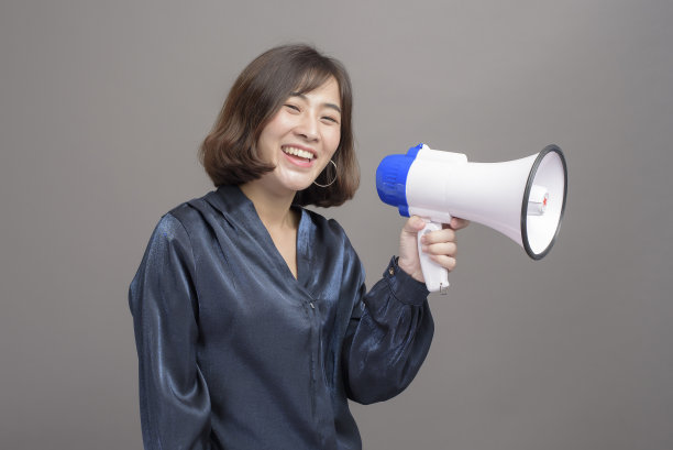 年轻美丽的亚洲女人的肖像在工作室背景上拿着扩音器。图片下载