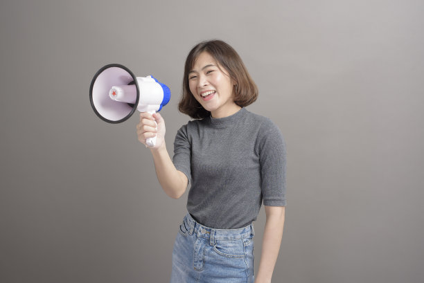 年轻美丽的亚洲女人的肖像在工作室背景上拿着扩音器。图片下载