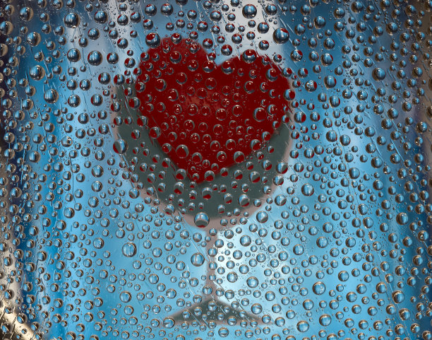 水滴位于蓝色背景上，配上一杯葡萄酒和心形轮廓的图片。特写镜头。图片下载