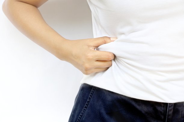 靠近胖胖的亚洲女人站着，用手把她的胖挤在白墙上有拷贝空间。观念超重应节食减肥以求健康。图片下载