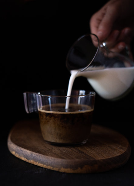 在黑色背景的木桌上，用手把牛奶倒进一杯咖啡里。图片下载