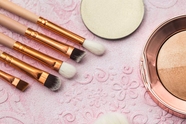 软化妆刷，烘焙粉和其他化妆品在米色的背景。从上往下看。图片下载
