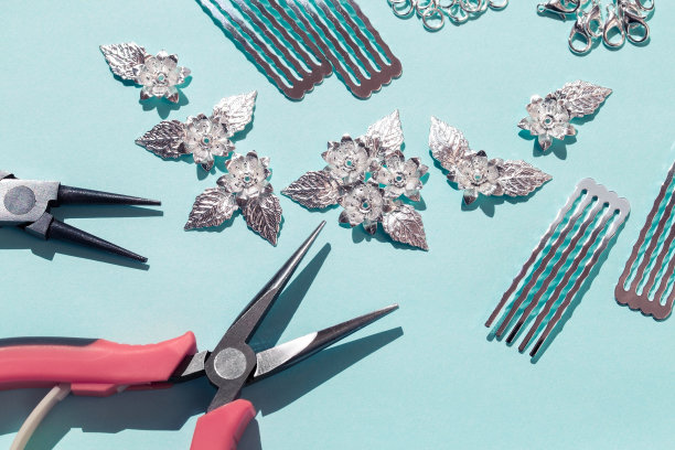 发饰的设计。用自己的双手创造珠宝。钳子，扇贝，金属首饰配件的形式的花和叶子在蓝色的背景图片下载