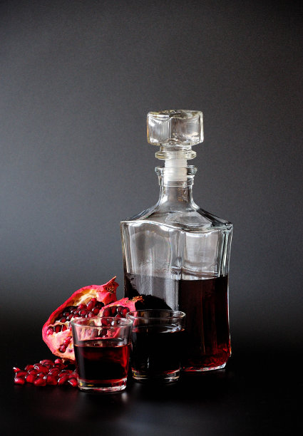 暗红色柳儿在一个瓶子和两个玻璃杯，旁边一个成熟的水果和石榴籽在黑色的背景。图片下载