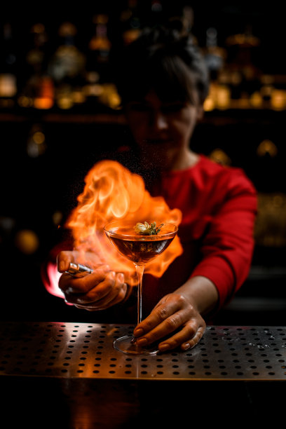 吧台上的酒杯，女调酒师准确地洒了几滴，然后点燃了图片下载