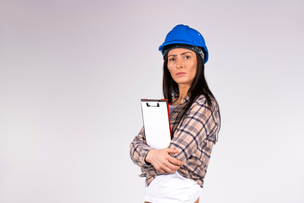 严肃的女工程师，手里拿着文件夹，看着灰色背景空白的相机。图片下载