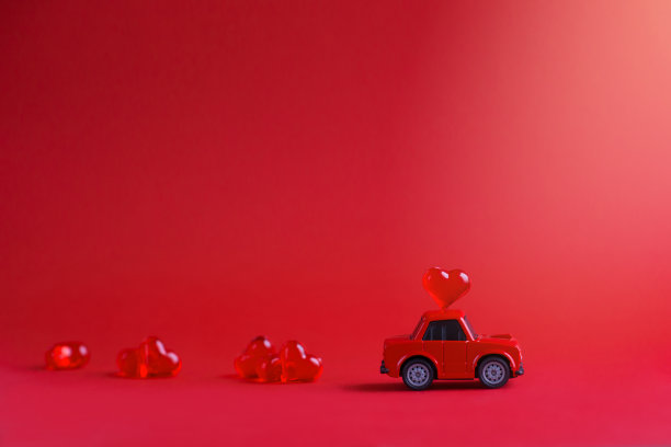 一辆红色的玩具车，在红色的背景下，在车顶上放着一列玻璃心。情人节的概念。横幅。水平格式。Copyspace图片下载