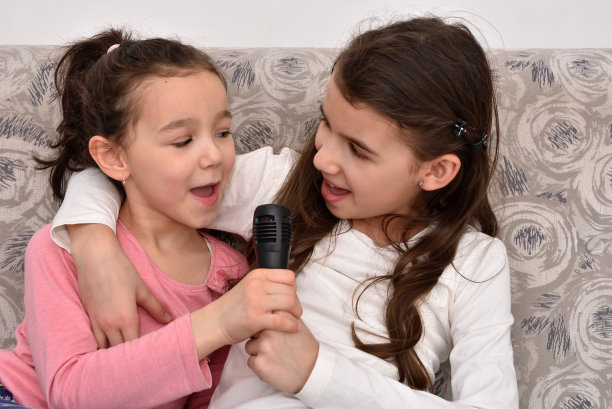 两姐妹拿着麦克风坐在沙发上唱歌图片下载