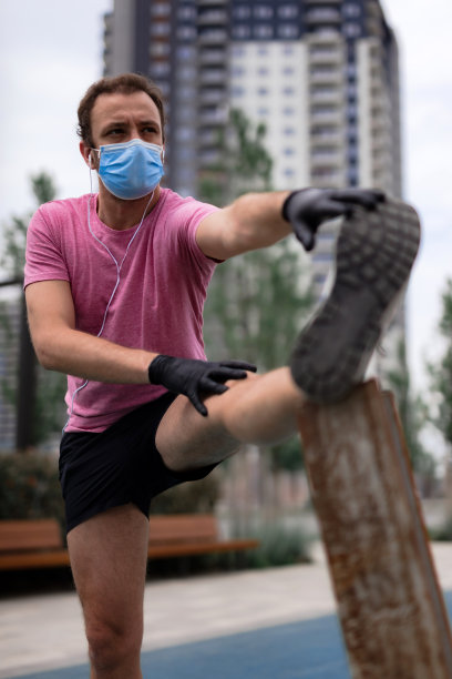 运动员戴着医用口罩和手套，智能手机和耳塞，在城市环境中慢跑。图片下载