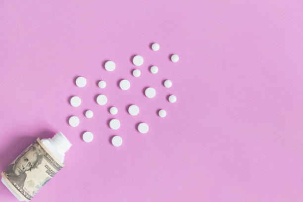 装有美元和各种白色药丸的药瓶。药品概念保险，药价高。孤立在粉红色的背景上。图片下载