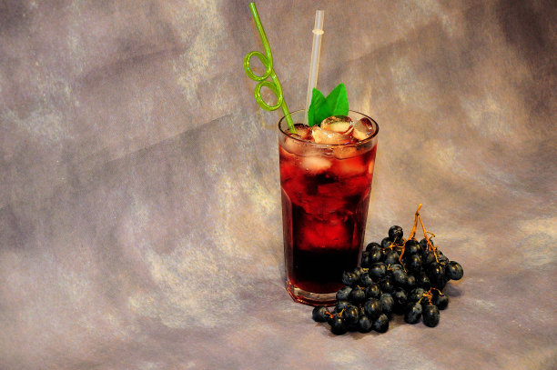 灰色的背景上，放着一个用深红色餐巾、冰和吸管的高杯，旁边是一堆红色的电影院。图片下载