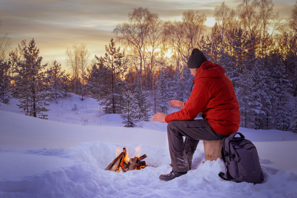 旅人坐在篝火旁，在雪地里暖手。图片下载