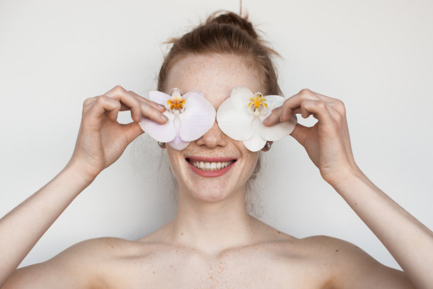 近距离的照片，一个白人妇女赤裸的肩膀覆盖她的眼睛与鲜花和微笑牙齿图片下载