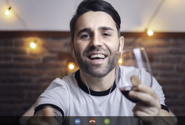 情人节当天，一个年轻男子在视频通话中，一边喝着红酒一边与女友聊天。Covid概念。图片下载