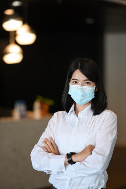 自信的女商人戴着防护面具，双手交叉站在现代办公室里的肖像。图片下载