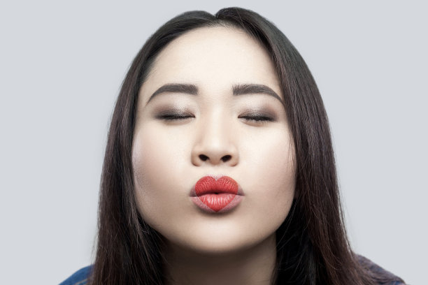 肖像在爱美丽的黑发亚洲年轻女子在休闲蓝色牛仔夹克与化妆站闭上眼睛和发送吻图片下载