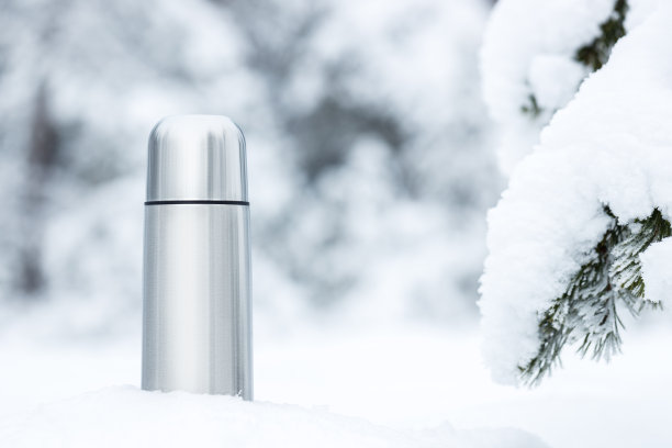 钢质保温瓶和美味的热茶在雪域森林的特写镜头。图片下载