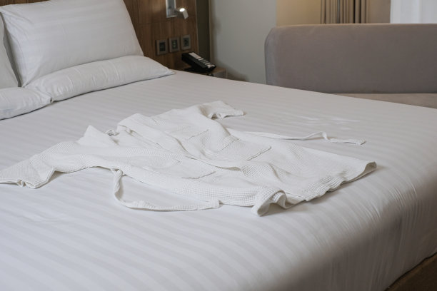 酒店床上的白色浴衣。酒店舒适的床和干净的浴袍。图片下载