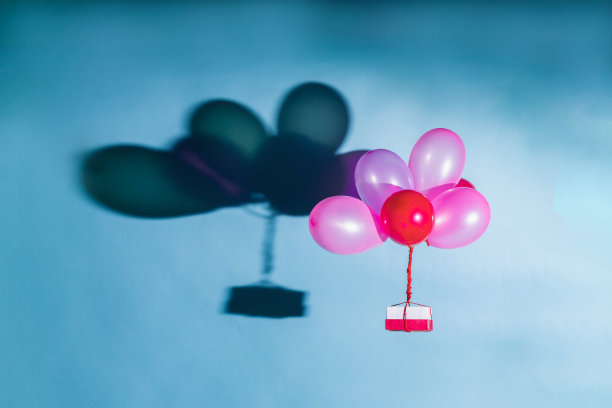 带着盒子的粉色气球在蓝色背景上飞行。一堆粉色和红色的飞球图片下载
