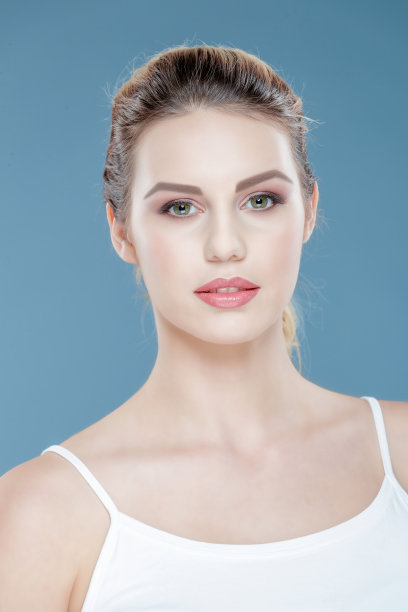 美丽的年轻女子在坦克上装摆出对蓝色背景图片下载